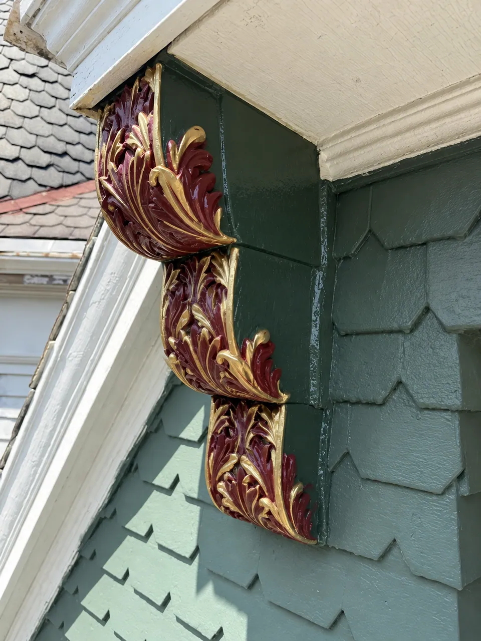 The same bracket painted: deep green sides, and the carved acanthus leaves in burgundy with gold edges, under the cream eave.