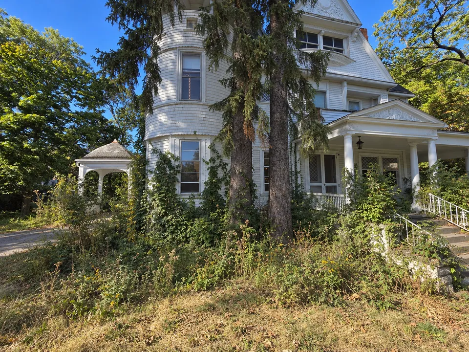 The tower side of the house as it was: weeds and vines over the foundation and the beds, and the lawn gone to seed.